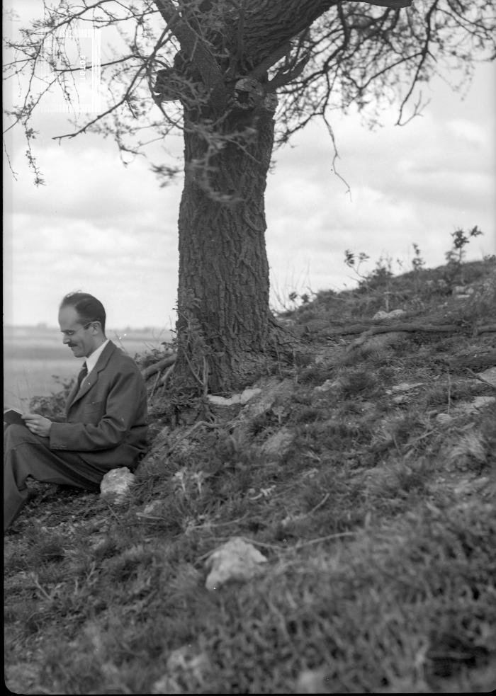 César C. Bustos leyendo junto a árbol
