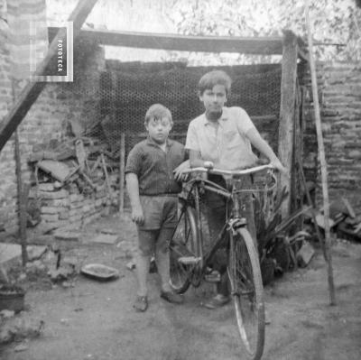 Raúl Oscar y César A. Bustos con bicicleta en fondo casa